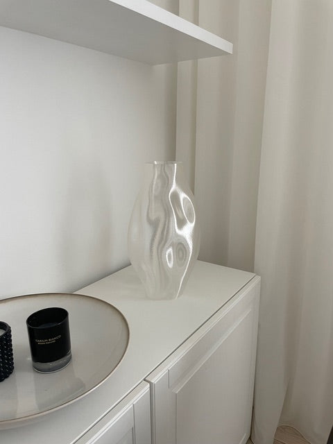 Illumina Vase i hvid bioplast elegant placeret på en hylde, perfekt til tørrede blomster eller som et dekorativt element i boligindretningen.