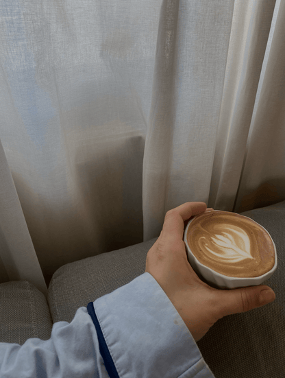 Hånd, der holder tidevandskoppen med skummende kaffe.