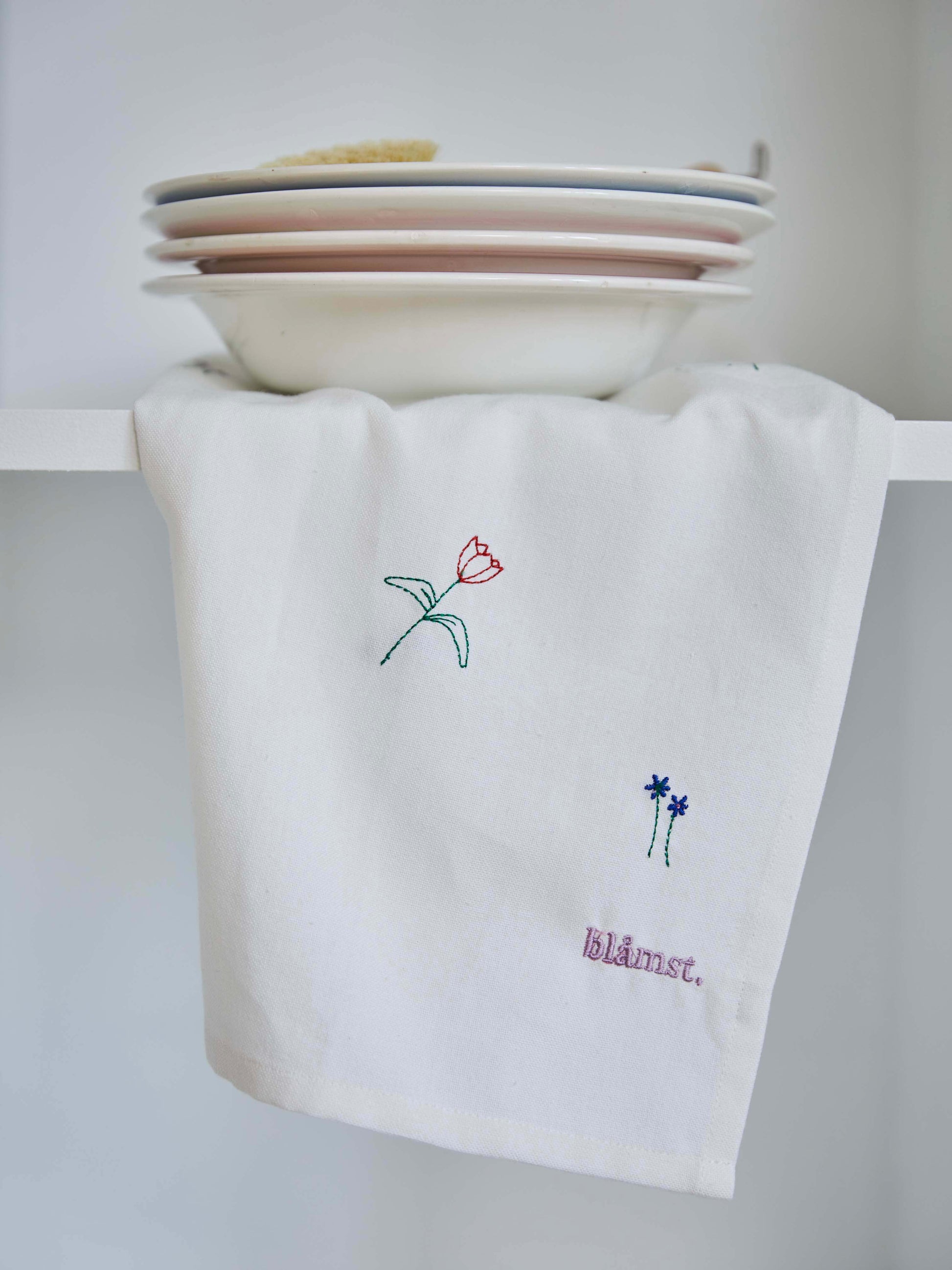 Blåmst Flower viskestykke med minimalistiske broderede markblomster og logo, skabt i GOTS-certificeret bomuld.