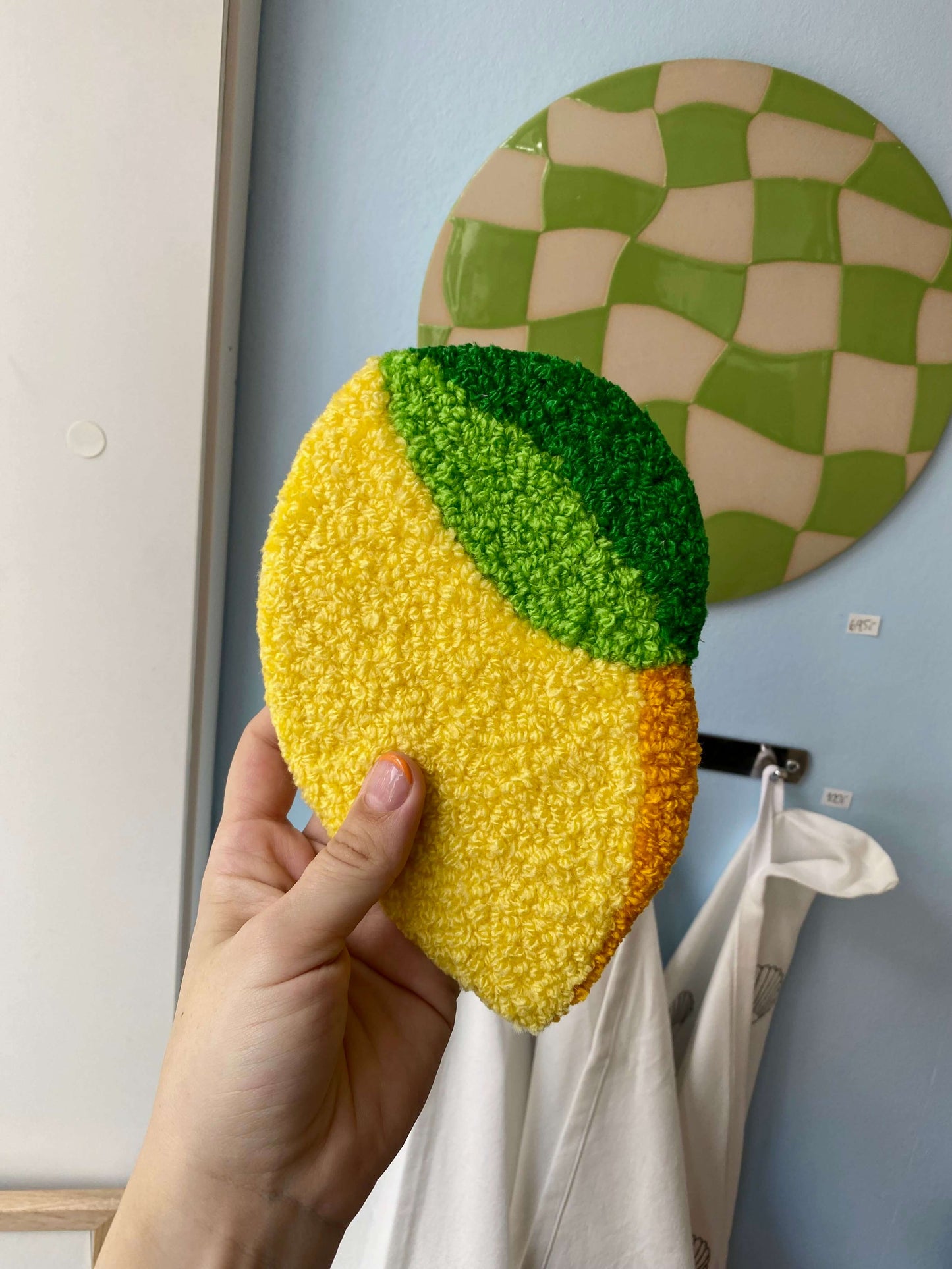 Håndlavet citron vægtæppe fra @riis.design hængt op på væggen – gul og grøn tufting.
