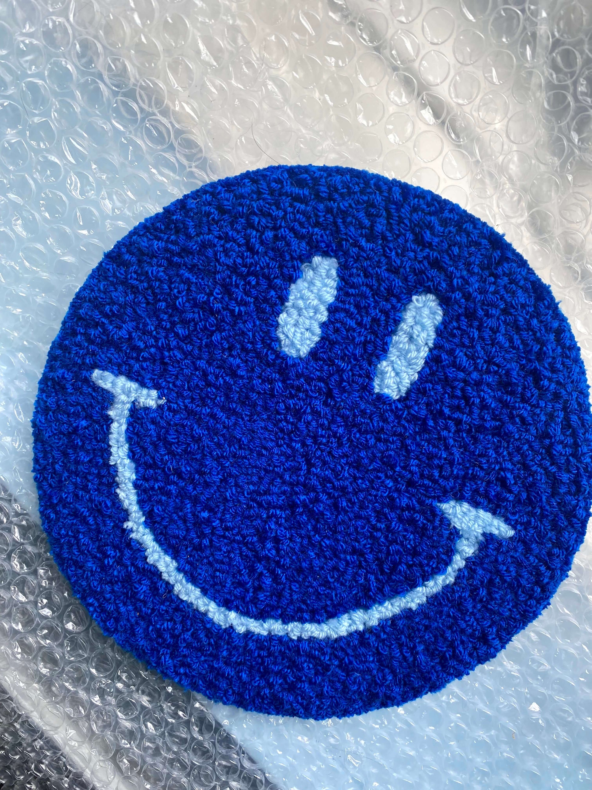 Blåt Smiley vægtæppe med mørkeblå ansigtstræk – på lilla underlag.
